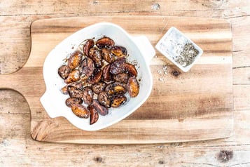 In Balsamico karamellisierte Kartoffeln liegen in einer weißen Schüssel, die auf einem Holzbrett steht,