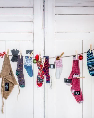 An einer Wäscheleine hängen Socken und Beutel mit Zahlen von 1 bis 24 als Adventskalender vor einer weißen Tür.