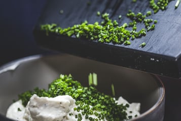 Schnittlauch wird in eine Schale mit hellem Dip gegeben