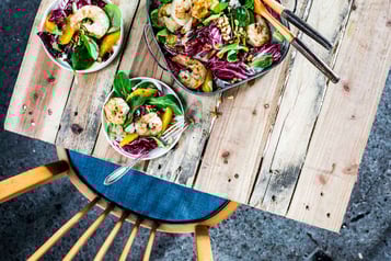 Auf einem Holztisch steht eine Schüsseln mit Salat, daneben zwei kleine Schüsseln mit Portionen