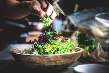 In einer Holzschale liegt geschnittener Salat. Währenddessen schneidet eine Schere weitere Salatblätter in die Schale.