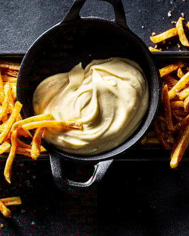 Cremige selbstgemachte Mayonnaise und Fritten vor dunklem Hintergrund