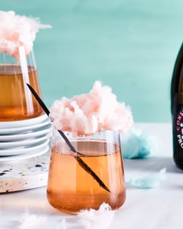Zwei Gläser mit Prosecco Rosé, die mit hellrosa Vanille-Zuckerwatte und einer Vanilleschote getoppt sind, vor weißem Untergrund und einer türkisen Wand.