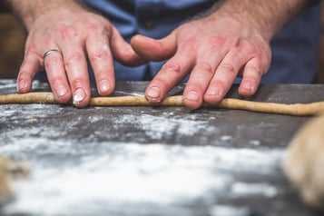 2 Hände rollen den Teig zu einem dünnen Schlauch auf einer grauen Arbeitsplatte.