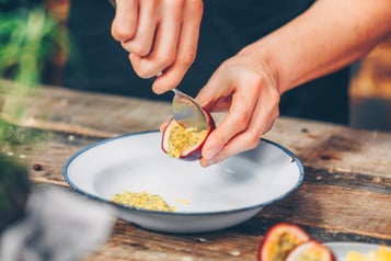 Aus einer Maracujahälfte wird mit einem Esslöffel das Fruchtfleisch ausgekratzt