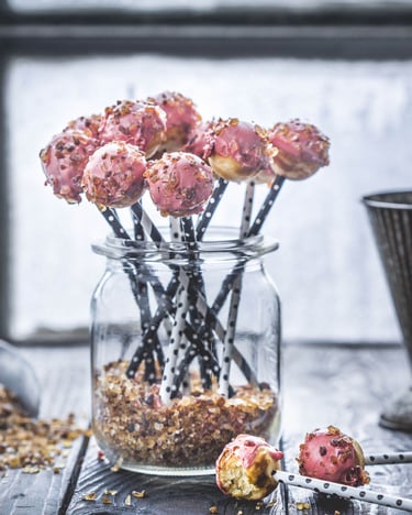 Ein Glas mit Cake Pops und eine Backschaufel mit Kandiszucker vor einem Fenster