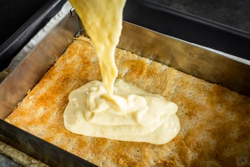 Auf den gebackenen Teig, der sich in einem Rahmen befindet, wird die Creme gegeben