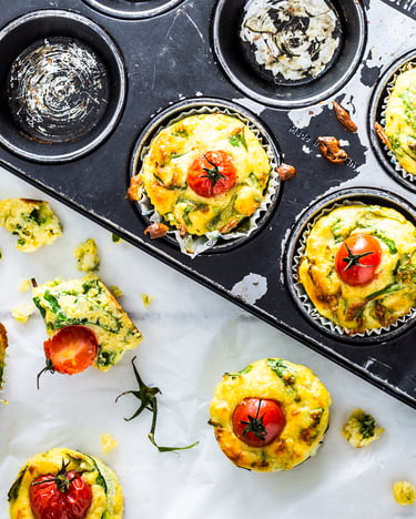 Gemüse-Muffins mit Kirschtomaten in einem Muffinblech und auf Backpapier