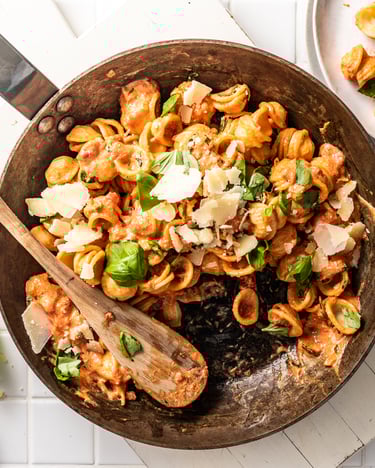 Pfanne mit Orecchiette mit Tomaten-Ricotta-Sauce, darin liegt ein Holzlöffel und daneben stehen Parmesan und liegt Basilikum