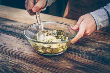 Die Marinade befindet sich in einer Glasschüssel und wird von einer Person mit einem Löffel verrührt.