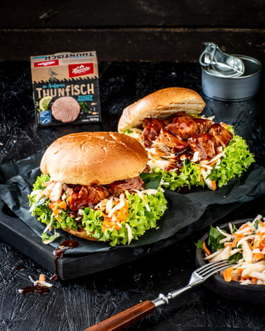 Zwei üppig belegte Burger mit Salat, Möhren und Thunfisch in Barbecue-Sauce sind auf schwarzem Untergrund präsentiert