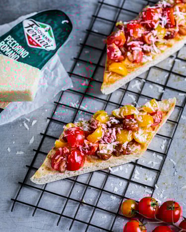 2 Stückchen Bruschetta mit Dattel-Tomaten-Topping und Pecorino auf hellgrauem Untergrund