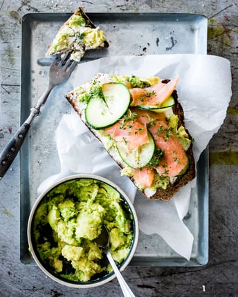 Stulle mit Avocado, Lachs und Gurke neben einer Schale mit Guacamole