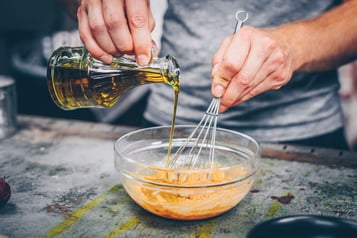 In einer Glasschüssel werden mehrere Zutaten zu Tahini-Dressing vermengt.