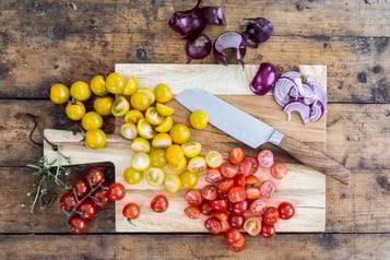 Gelbe und rote Cherrytomaten halbiert auf einem Holzbrett, daneben einige Zwiebelringe