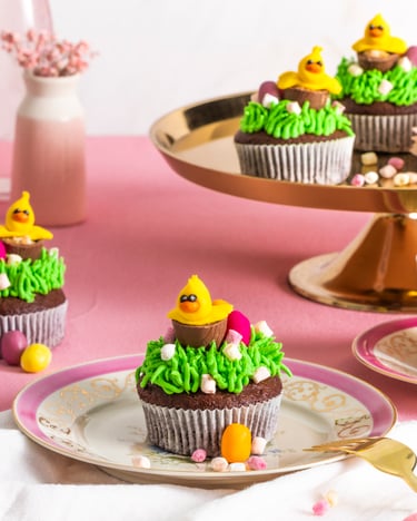 ein Oster-Muffin steht auf einem Teller, weitere stehen daneben und auf einer Etagere