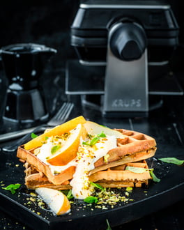 Chaiwaffeln mit Gewürzbirne vor drehbarem Krups Waffeleisen Professional, auf dunklem Teller vor dunklem Hintergrund.