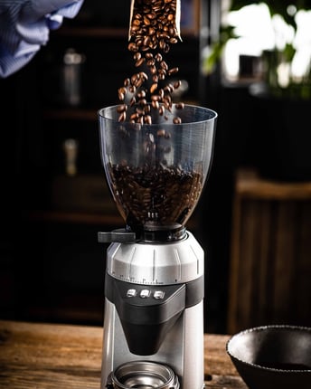 Kaffeebohnen werden aus der Packung direkt in eine elektrische Kaffeemühle gegeben