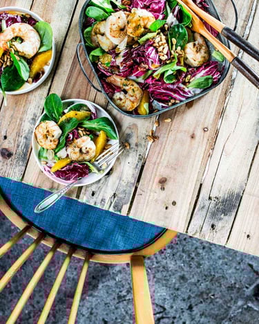 Auf einem Holztisch steht eine Schüsseln mit Salat, daneben zwei kleine Schüsseln mit Portionen
