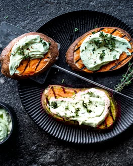 Drei Süßkartoffel-Steaks mit Avocado-Creme auf einem schwarzen Teller vor dunklem Hintergrund