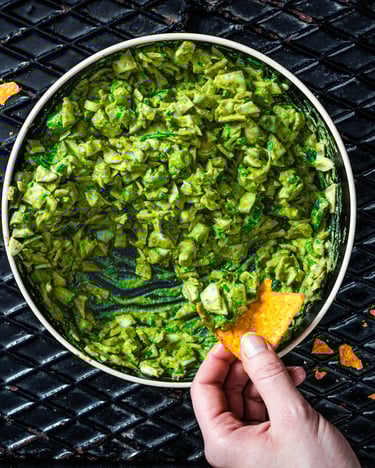 Eine Schale mit leuchtend grünem Green Goddess Salad, der mit Tortilla-Chips weggesnackt wird