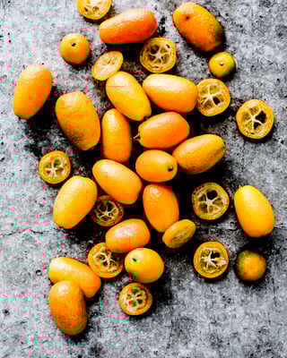 Kumquats ganz und aufgeschnitten auf grauem Untergrund