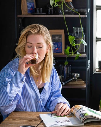 Stylistin Jules genießt ein Glas schwarzen Kaffee und blättert dabei entspannt in einem Magazin