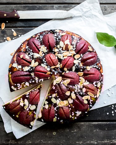 Ein angeschnittener Pflaumenkuchen auf einem weißen Papier auf dunklem Holz