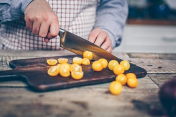 Gelbe Cherrytomaten werden auf einem dunklen Holzbrett mit einem großen Messer halbiert
