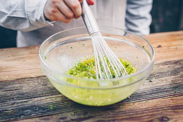 In einer Schüssel befindet sich das Kräuter-Vinaigrette und wird mit einem Schneebesen vermengt.