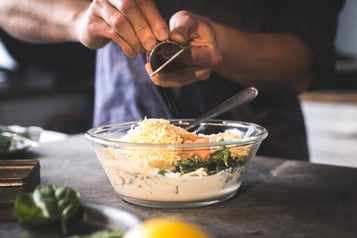 Muskatnuss wird in eine Schale mit Frischkäsemasse, Spinat, Lachs und geriebenem Käse gerieben