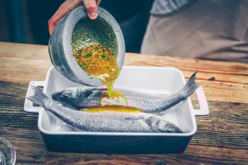 Die Marinade wird aus einer Schale über den Fisch gegeben.
