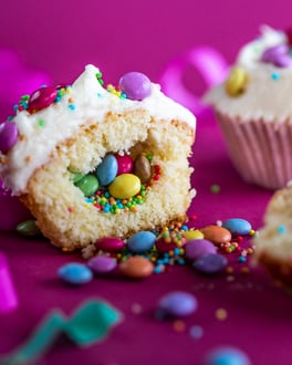 Cupcakes mit Smarties-Füllung auf pinkem Untergrund