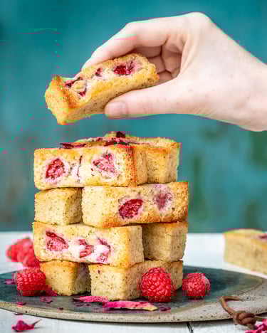 Die kleinen mit Himbeeren gefüllten Küchlein sind auf einer runden Platte wie Jenga-Steine aufeinander gestapelt. Ein Kuchen wird gerade vom Stapel genommen.