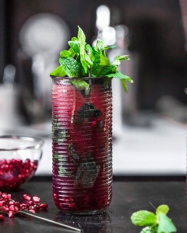 2 Gläser Alkoholfreier Granatapfel Mojo stehen auf einem schwarzen Untergrund. Daneben eine Schale mit Granatapfelkernen