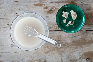 Eine Schüssel mit einem Schneebesen in Milch steht neben einer Schüssel mit Hefe