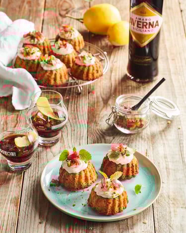 Viele Mini-Gugelhupfe mit Ricottacreme auf Holzuntergrund, daneben stehen Gläser und eine Flasche Averna