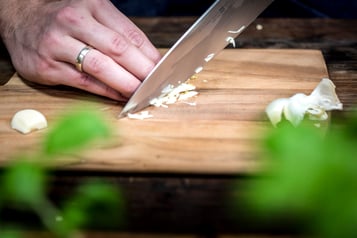Auf einem Holzbrett wird Knoblauch fein gehackt