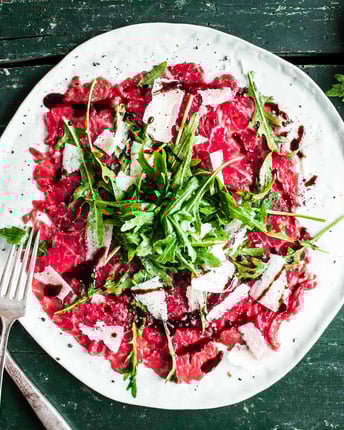 Auf einem weißen Teller Carpaccio angerichtet mit Parmesan und Rucola