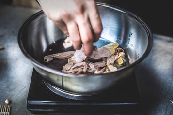 In einer silbernen Küchen-Schüssel liegen Entenbrustfilets, die infeine Streifen geschnitten werden.