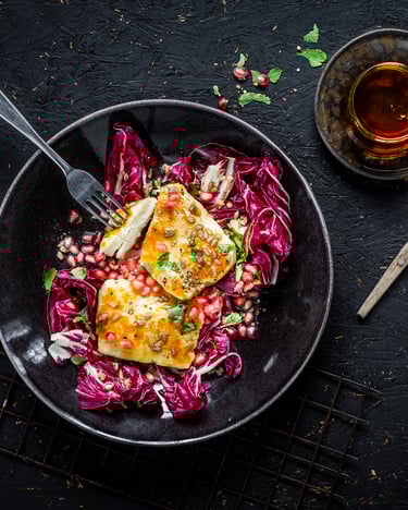 Gebackener Halloumi auf einem Teller mit Radicchio und Granatapfelkernen mit einer Gabel.