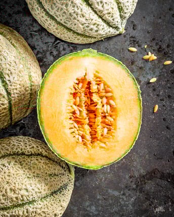 Ganze und halbierte Cantaloupe-Melone als Topshot von oben auf dunkelgrauem Untergrund