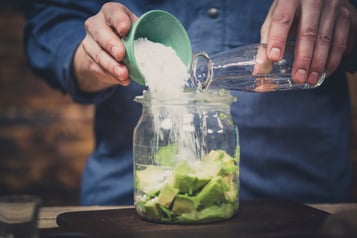 In einem Glas liegt Avocado, in das Puderzucker und Zitronensaft hinzugegeben werden.