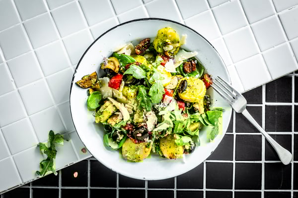 Ein großer Teller mit buntem Kartoffelsalat ist von oben auf schwarzen und weißen Kacheln fotografiert, die sich schräg durch das Bild ziehen.