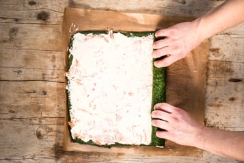 Mit Lachs und Creme bestrichene Spinatmasse wird auf einem Backpapier zu einer Rolle aufgerollt