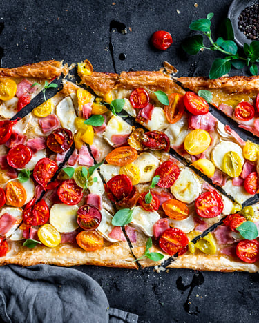 Auf schwarzem Untergrund liegt eine in Stücke geschnittene Tomaten-Quiche vom Blech