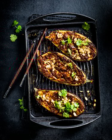 Auf schwarzem Untergrund liegen Miso-Auberginen mit Erdnüssen.