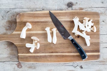 Pilze liegen auf einem Holzbrett zusammen mit einem Messer
