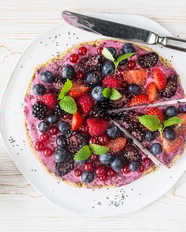 Auf einem weißen Teller auf weißem Holzuntergrund liegt eine mit Beeren und Minze süß-belegte Pizza. Daneben eine kleine Schale mit Chiasamen