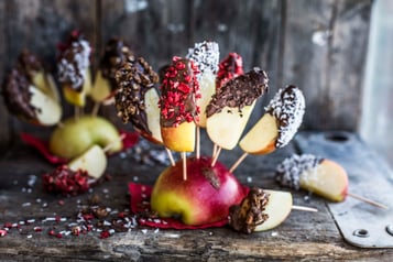 in einen halben Apfel sind mehrere Apfelspalten mit Schokolade überzogen auf Spieße gesteckt